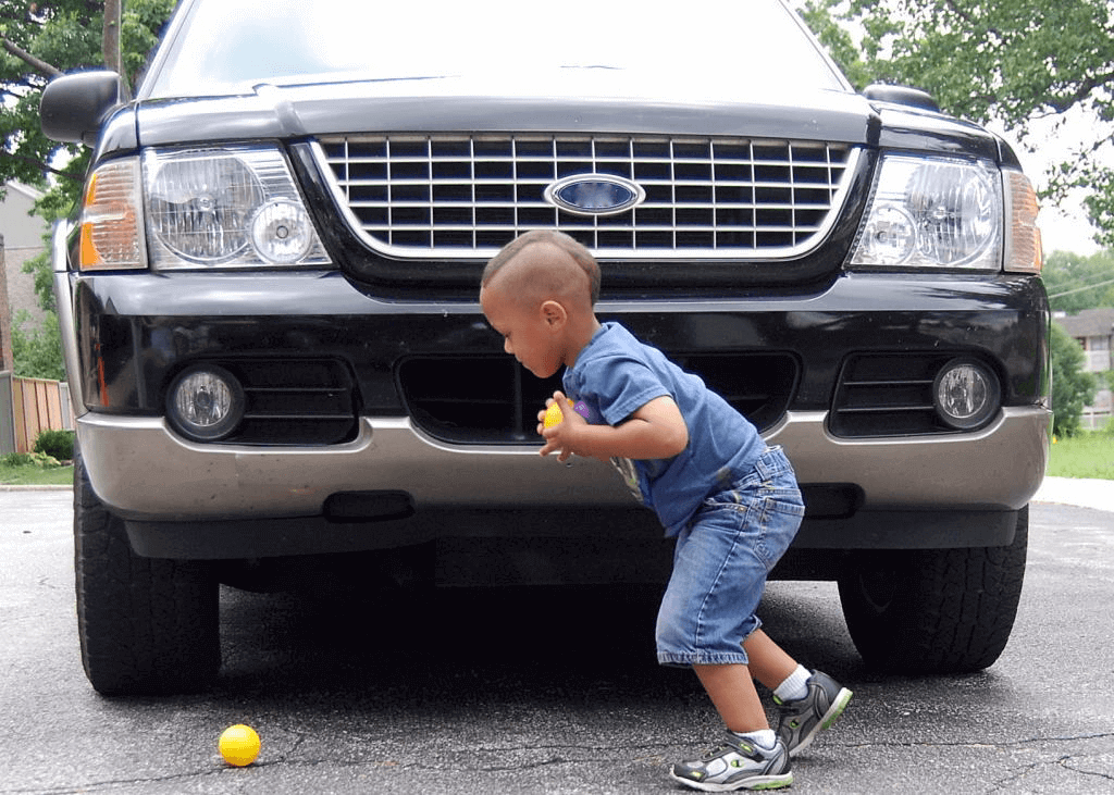 little boy picking up balls in front of vehicle