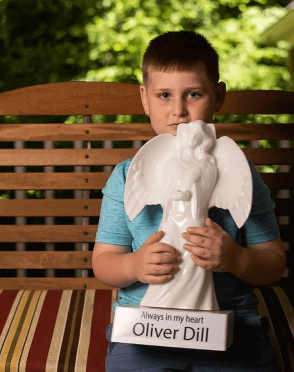 Owen Dill, 7, holds a memorial angel in honor of his younger brother Oliver that sits outside his home in Evansville, Ind., Wednesday, June 16, 2021. His brother Oliver, also known as "Ollie," died in 2019 after accidentally being forgotten in a car on the University of Southern Indiana campus. 