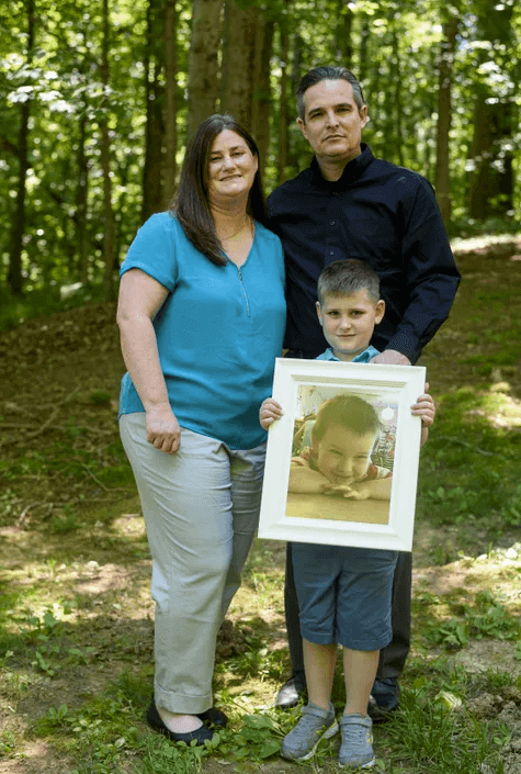 Jamie, Andrew and seven-year-old Owen Dill stand with a framed photo of Oliver in their backyard on the west side of Evansville, Ind., Wednesday, June 16, 2021. The Dills' three-year-old son Oliver, also known as "Ollie," died in 2019 after accidentally being forgotten in a car on the University of Southern Indiana campus.