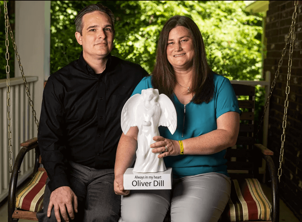 Andrew and Jamie Dill pose for a portrait with a memorial angel in honor of their son Oliver.